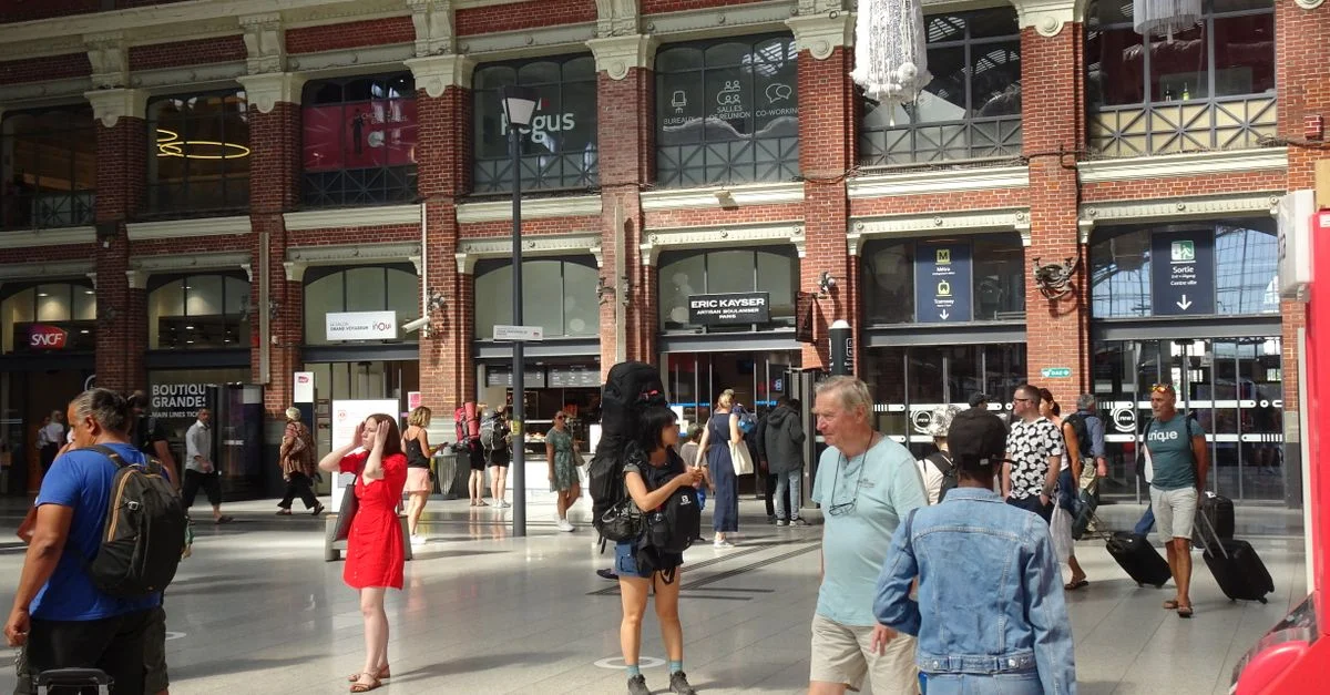 Des voyageurs à la gare d'Amiens, témoins de la vie citadine animée par une belle journée d'été.