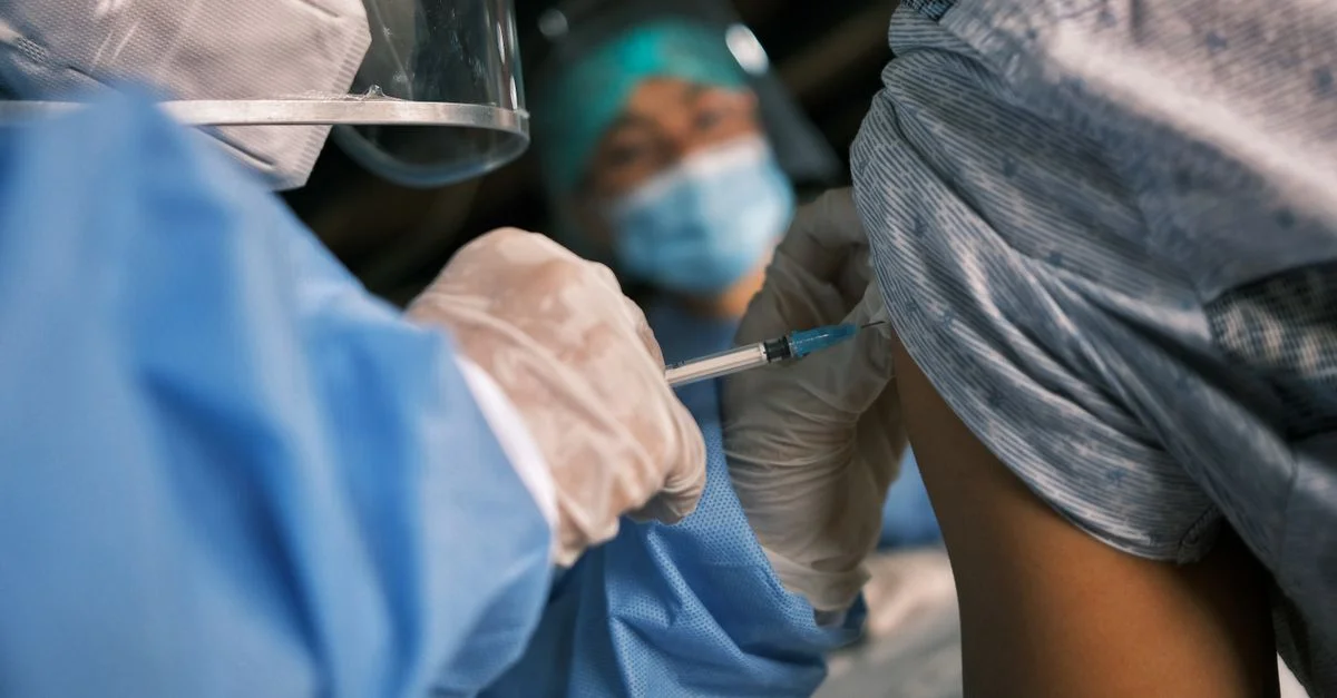 Un professionnel de la santé portant un équipement de protection administrant une vaccination à un patient.