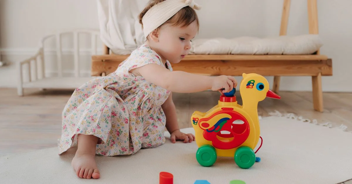 Une mignonne petite fille en robe à fleurs jouant avec un jouet canard coloré à l'intérieur.