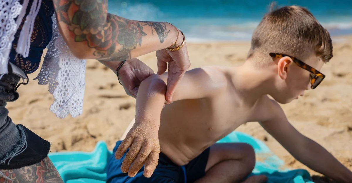Un enfant applique de la crème solaire lors d'une journée ensoleillée à la plage, assurant la protection de la peau.