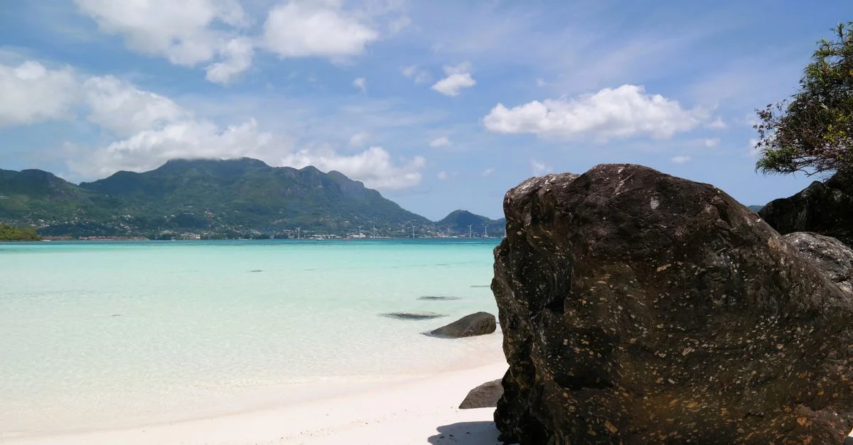 Une vue époustouflante d'une plage tropicale avec des eaux cristallines, un ciel bleu et des montagnes lointaines.