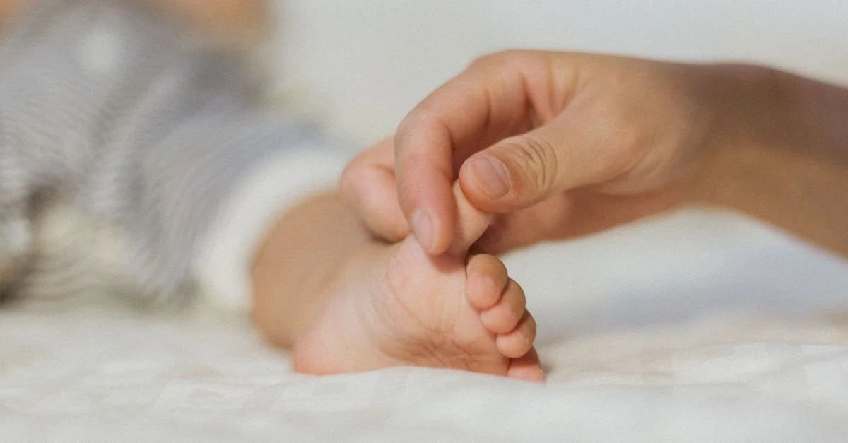Gros plan sur la main d'un parent tenant délicatement le pied d'un bébé, symbolisant l'amour et l'attention.