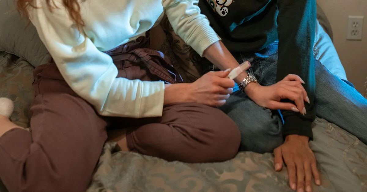 Un couple assis sur un lit, partageant un résultat positif de test de grossesse dans un cadre confortable et intime.