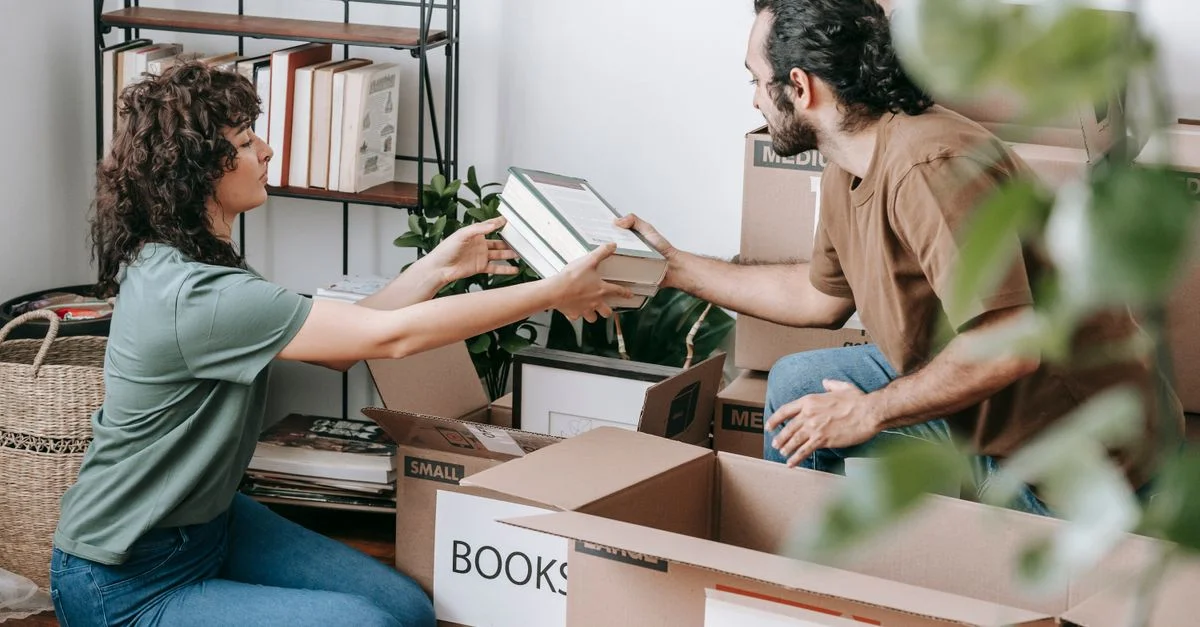 Un couple organisant et emballant des livres dans des cartons à l'intérieur, se préparant à un déménagement.