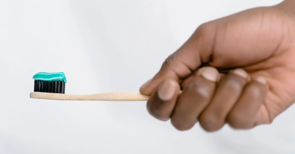 Main tenant une brosse à dents en bambou avec du dentifrice vert, mettant l'accent sur l'hygiène bucco-dentaire.