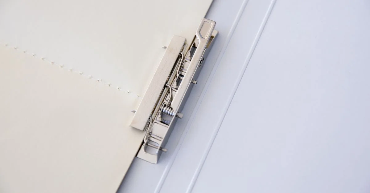 Un classeur en métal maintient des feuilles de papier, offrant une solution de bureau minimaliste.