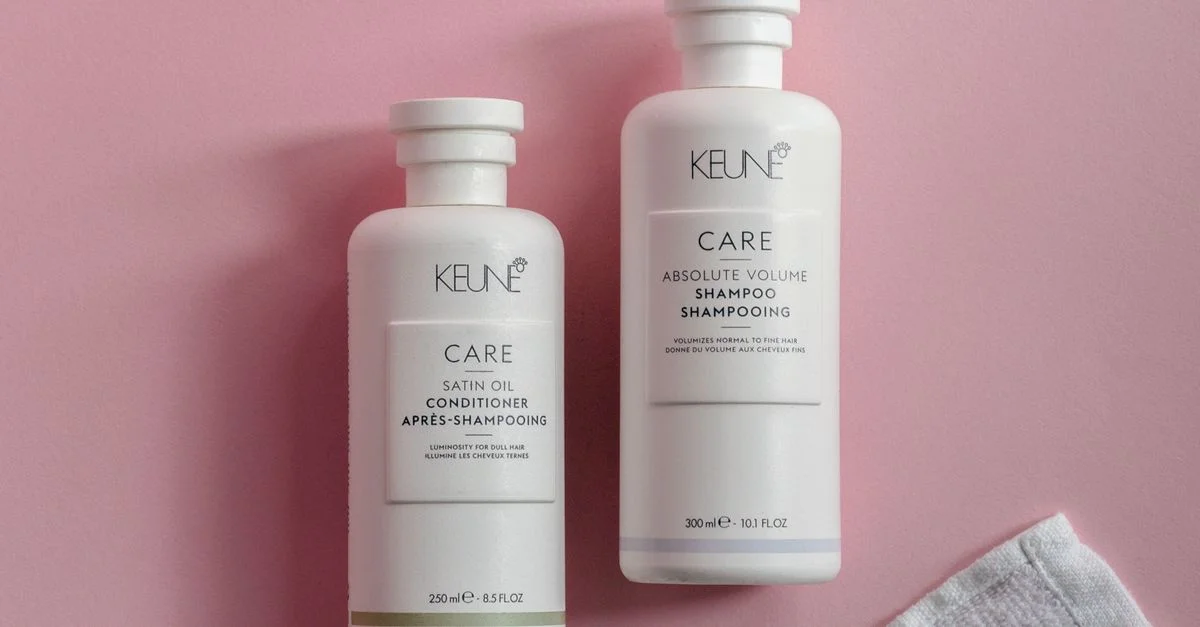 Vue en plongée de bouteilles de shampoing et d'après-shampoing sur un fond rose avec une serviette.