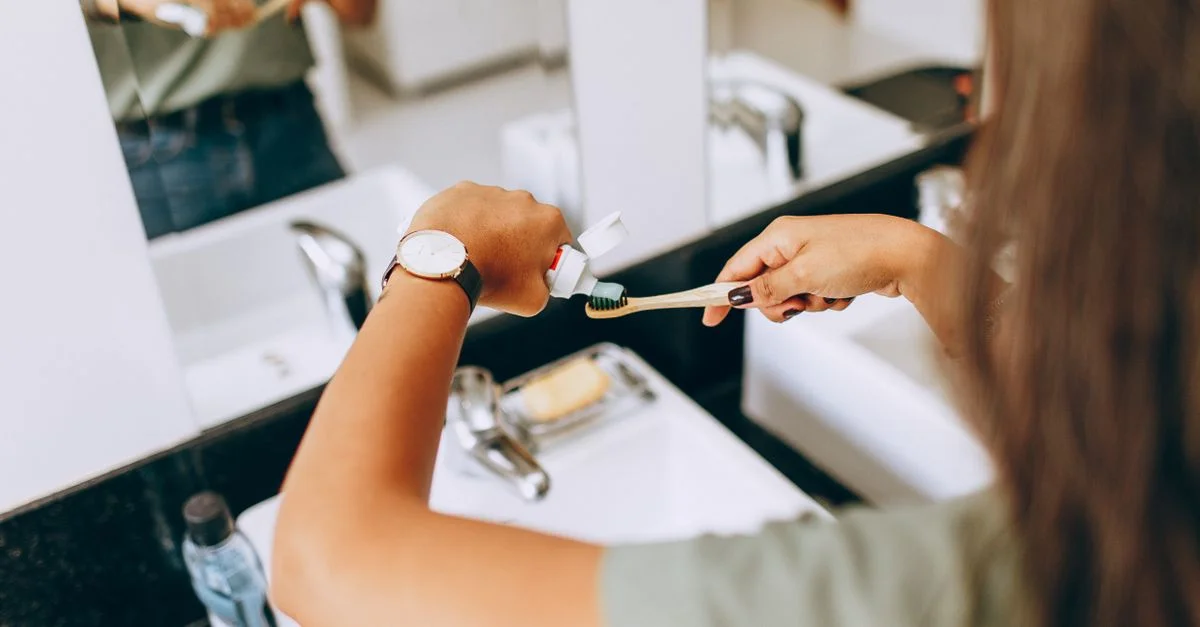 Une femme applique du dentifrice sur une brosse à dents dans une salle de bain, illustrant les habitudes quotidiennes d'hygiène bucco-dentaire.